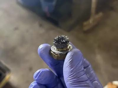 Close-up of oil drain plug with metal debris and contamination from pump during servicing of a Nilfisk SH Truck Booster, indicating wear inside the pump.
